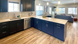 A modern kitchen with dark blue cabinets, a stainless steel dishwasher, and a marble countertop. - Pristine Home Near Sun Valley (Hailey)