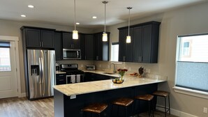 A modern kitchen with dark cabinets, stainless steel appliances, a marble countertop, and a central island with bar stools. - Pristine Home Near Sun Valley (Hailey)