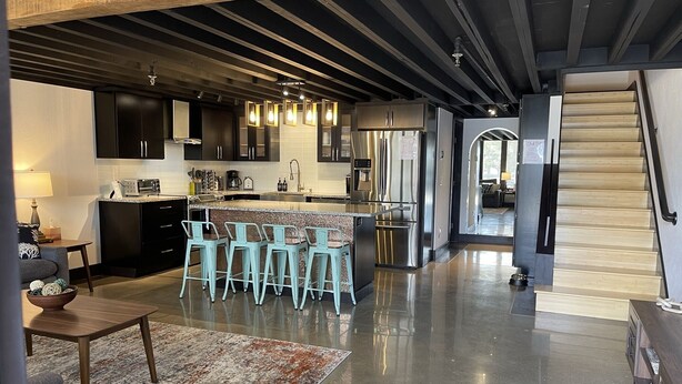 A modern kitchen with a central island, bar stools, stainless steel appliances, and a staircase leading to another level. - Golf Getaway with Golf Cart on Grand Lake in Shangri-La (Afton)