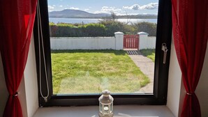 Ein Fenster mit Blick auf einen grünen Rasen, ein rotes Tor und ein Gewässer mit Bergen in der Ferne.