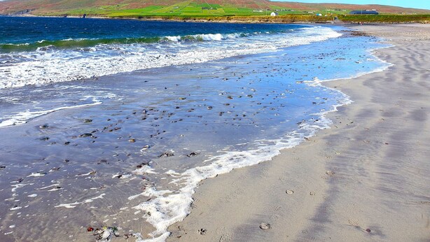 Ein Strand mit Wellen, ein Berg in der Ferne und ein klarer Himmel.