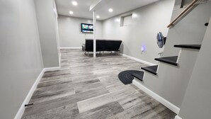 Un corridoio con tappeto grigio, una sedia nera, una TV fissata al muro e una piccola finestra.