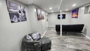 Un'area reception con un divano nero, una poltrona con motivo e una TV appesa al muro.