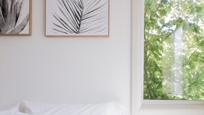 Ein Schlafzimmer mit einem Bett, weißen Wänden und zwei gerahmten Kunstwerken mit Blattformen.