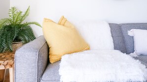 Ein graues Sofa mit einer weißen Tagesdecke, einem gelben Kissen und einem weißen Kissen. Ein runder Spiegel befindet sich über dem Sofa an der Wand.