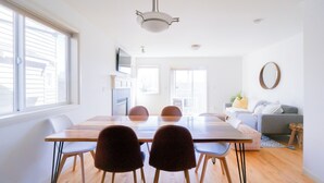 Ein modernes Wohnzimmer mit Essbereich, großen Fenstern, einem grauen Sofa und einem Holzesstisch mit Stühlen.