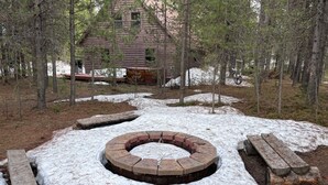 Eine rustikale Holzhütte, umgeben von einer verschneiten Landschaft, mit einem runden Feuerkorb und Holzbanken.