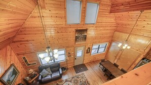 Ein gemütliches Blockhaus-Interieur mit Holzbalkendecke, Kamin, einer Couch und einem Essbereich.