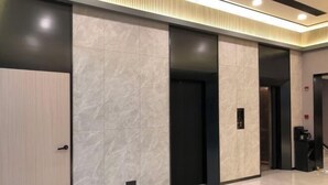 A modern hallway with a marble wall, a door, and an elevator. - Jingying Hotel (Kunshan)