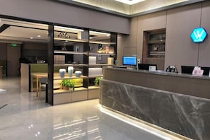 Zona de recepción de un hotel con mostrador de mármol, un escritorio y una exhibición de objetos decorativos.