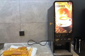 Eine Kaffeemaschine mit digitalem Display, eine Arbeitsplatte mit Papierkorb und eine Wand mit Fliesenmuster.
