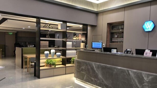 A modern reception area with a marble counter, a computer monitor, and a logo on the wall. - Jingying Hotel (Kunshan)