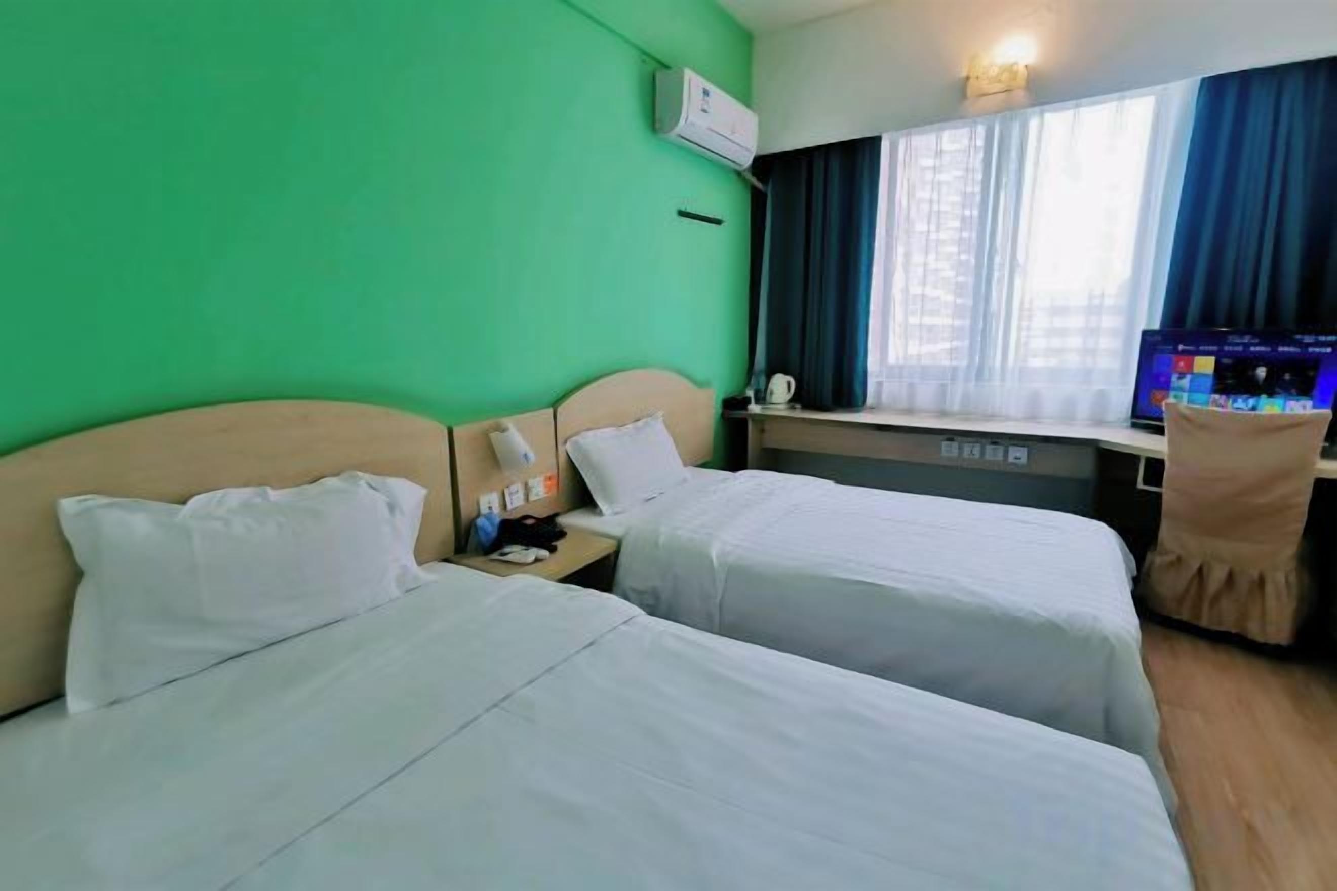 Habitación de hotel con dos camas, un escritorio con ordenador y una ventana con cortinas.