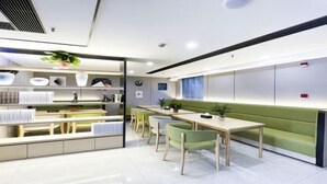 A modern, well-lit room with a long table and chairs, a green sofa, and a shelf with various items. - Jingying Hotel (Kunshan)