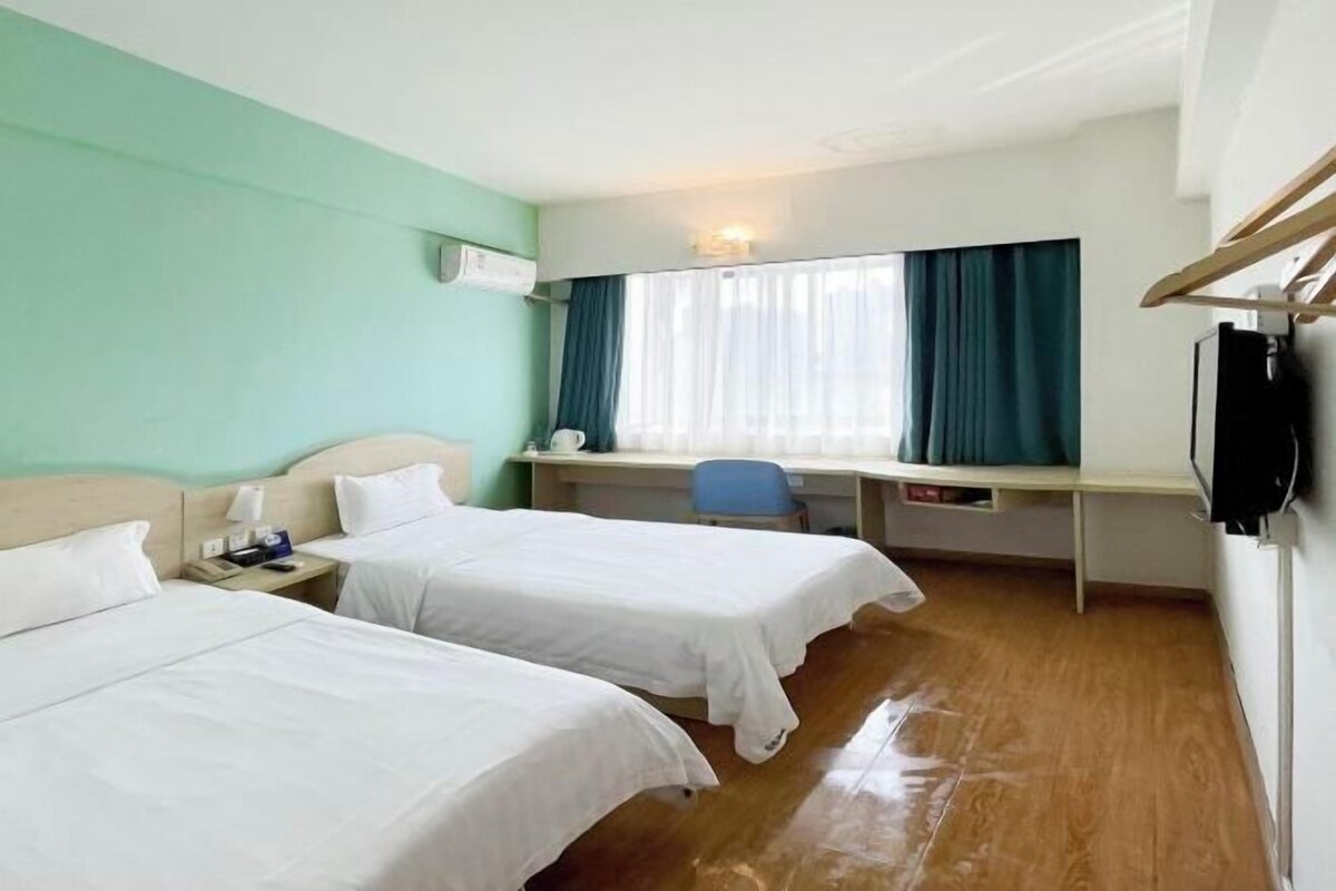 A hotel room with two beds, a desk, a chair, and a TV.