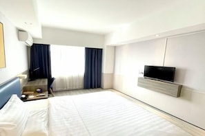 A hotel room with a bed, a TV mounted on the wall, a desk with a chair, and a window with curtains. - Jingying Hotel (Kunshan)