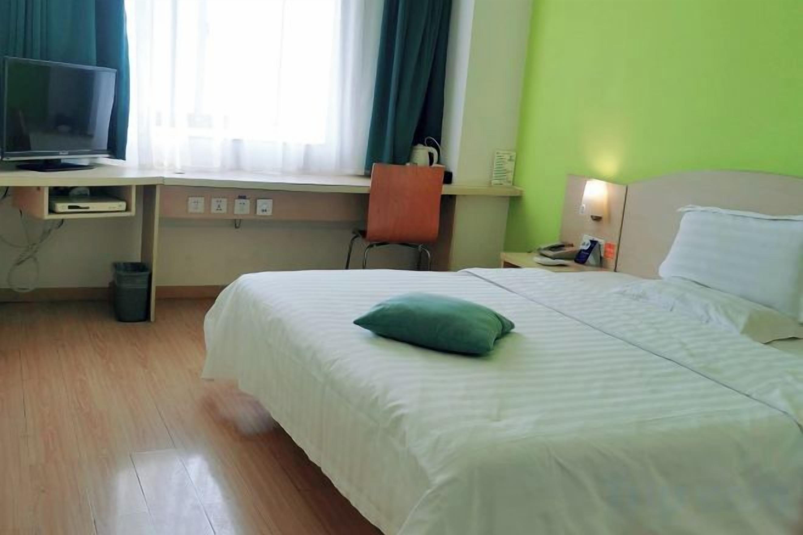 A hotel room with a bed, a desk with a computer, a chair, and a TV.