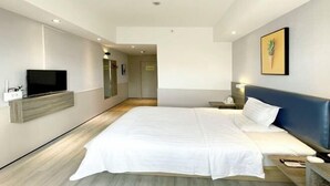A modern hotel room with a large bed, a flat-screen TV mounted on the wall, a bedside table, and a nightstand. - Jingying Hotel (Kunshan)