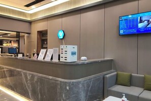 A hotel reception area with a marble counter, a digital screen displaying information, and a sofa with a pillow. - Jingying Hotel (Kunshan)