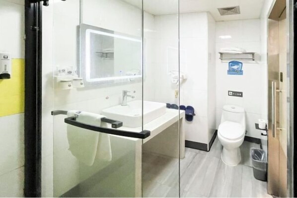 A compact bathroom with a glass partition, a sink, a mirror, a toilet, and a trash bin. - Jingying Hotel (Kunshan)