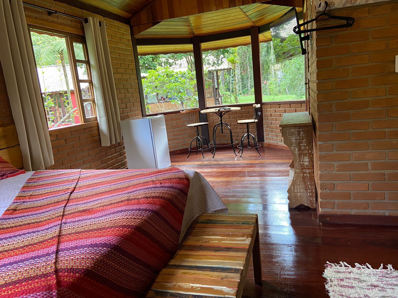 A cozy room with a bed, a small table, and chairs, a refrigerator, and a view of greenery outside.