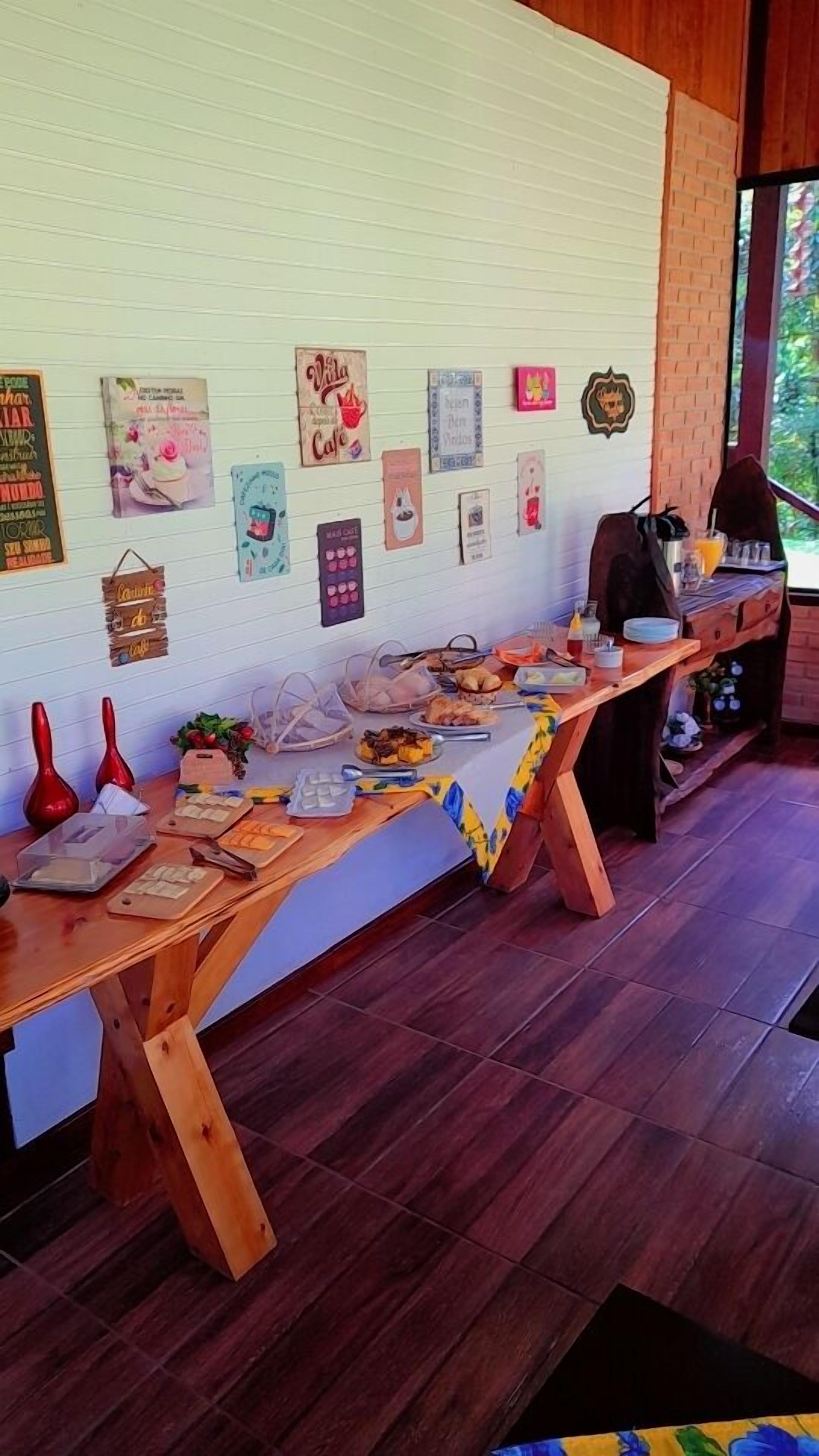 A long wooden table with various food items and a drink, set against a white wall with multiple framed pictures.