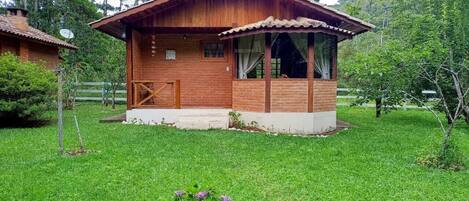 Una cabaña de madera con techo de tejas, rodeada de exuberante vegetación y un césped bien cuidado.