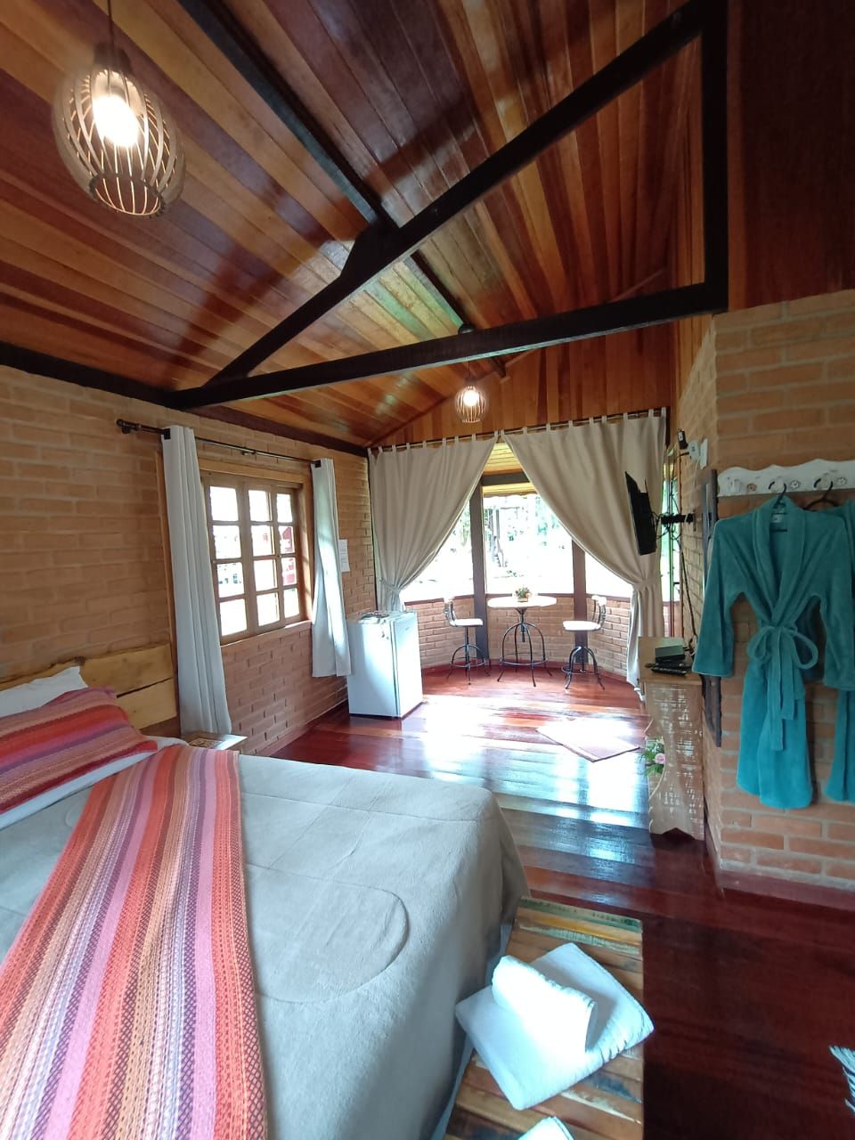 A room with a bed, a small table, a chair, a window with curtains, and a view of the outdoors.