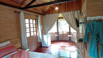 A room with a bed, a small table, a chair, a window with curtains, and a view of the outdoors.