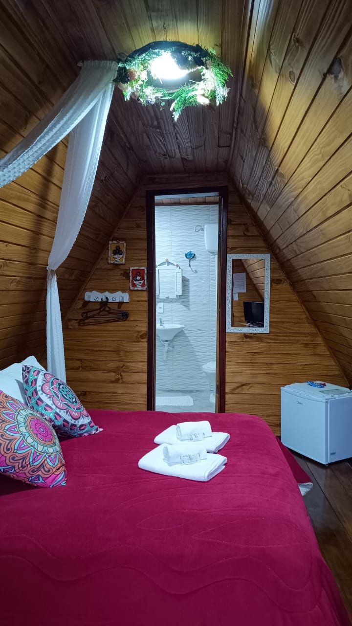 A cozy attic bedroom with a red bedspread, a canopy bed, and a small white refrigerator.
