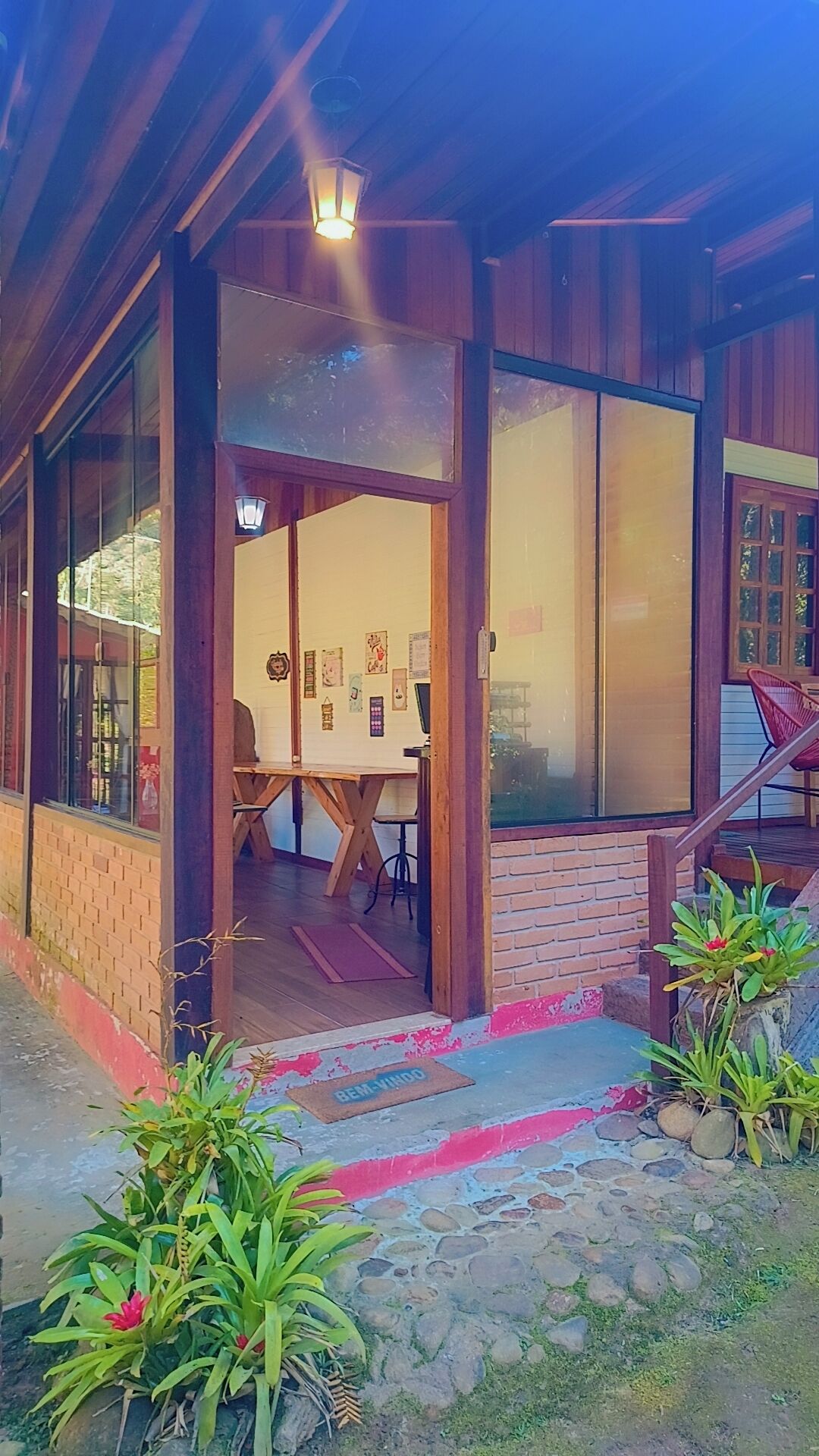 A wooden building with a covered entrance, a dining area with a table and chairs, and a stone pathway leading to the entrance.