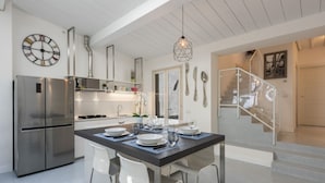 A modern kitchen with a stainless steel refrigerator, a dining table set for four, and a staircase leading to an upper level. - Apartments Florence - Oltrarno Garden (Firenze)