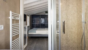 A modern bathroom with a glass shower enclosure, a visible towel rack, and a bed in the adjacent room. - Apartments Florence - Oltrarno Garden (Firenze)