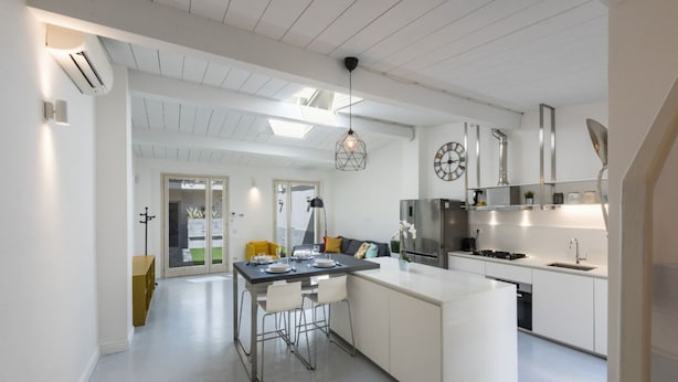 A modern kitchen with white cabinetry, a central island, and a dining area with chairs. - Apartments Florence - Oltrarno Garden (Firenze)