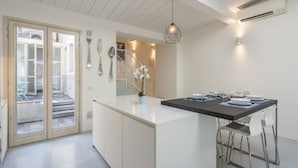 A modern kitchen with a central island, white cabinetry, and a dining area with a table set for four. - Apartments Florence - Oltrarno Garden (Firenze)