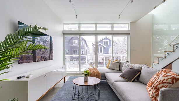 Ett modernt vardagsrum med ett stort fönster, en grå soffa, ett soffbord och ett vitt skåp.