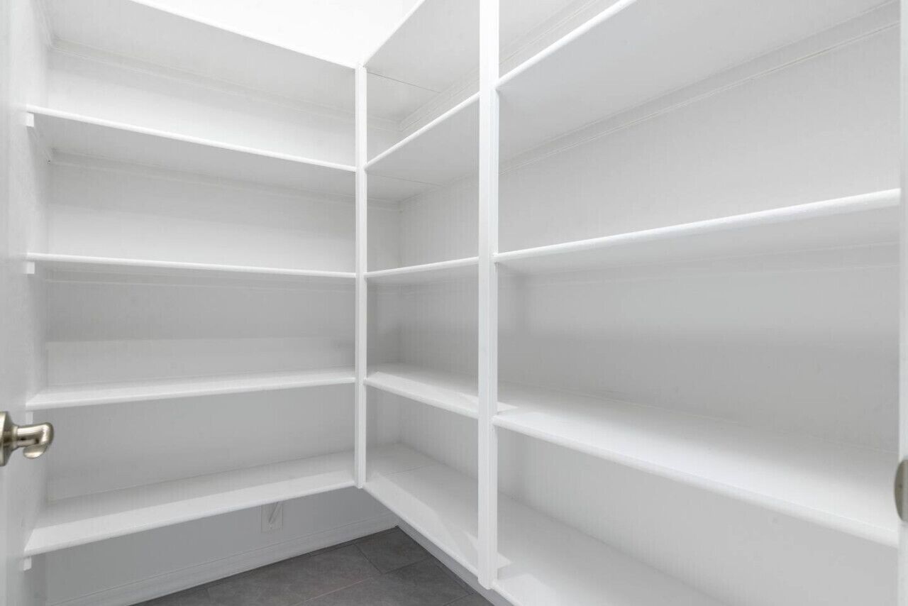 A corner closet with white shelving units and a door.