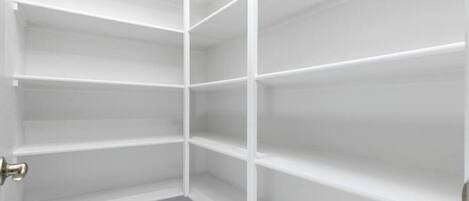 A corner closet with white shelving units and a door.