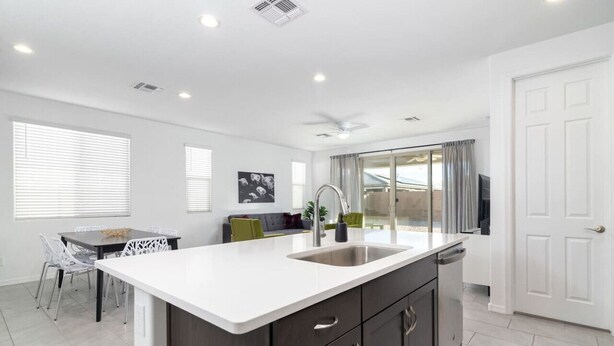 Una cocina moderna con una isla grande, encimeras blancas, muebles oscuros y una zona de comedor con mesa y sillas.