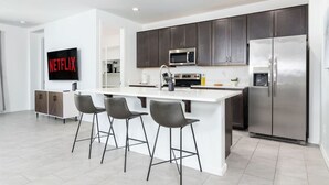 Una cocina moderna con una isla central, taburetes de bar, un refrigerador grande y un microondas.