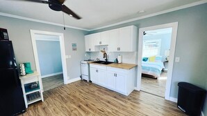 A compact kitchen with white cabinets, a stove, and a ceiling fan. - The Bungalow on Betty (Clearwater)