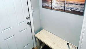 A hallway with a white door, a small wooden bench, and three framed sunset pictures on the wall. - The Bungalow on Betty (Clearwater)