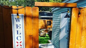 A wooden gate with a 'WELCOME' sign and a 'YOU ARE SOMEBODY'S REASON TO SMILE' sign in a backyard. - The Bungalow on Betty (Clearwater)