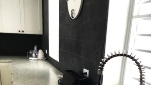 Una cocina con un lavamanos negro, un grifo de acero inoxidable, una encimera blanca con vetas y un salpicadero negro.