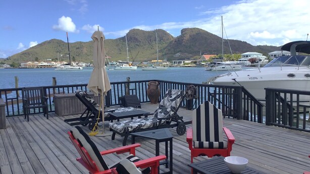 Una terraza con mobiliario exterior, una mesa y vistas al puerto deportivo y las montañas.