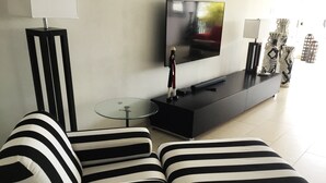 Una sala de estar moderna con un sofá a rayas negras y blancas, una mesa de centro de vidrio, un televisor de pantalla plana y un mueble de entretenimiento negro.