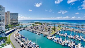 Un port de plaisance où sont amarrés de nombreux bateaux, un parking et, au fond, un grand bâtiment d’hôtel.