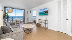 Un salon moderne avec vue sur l’océan, une table ronde, un canapé et un tableau accroché au mur.
