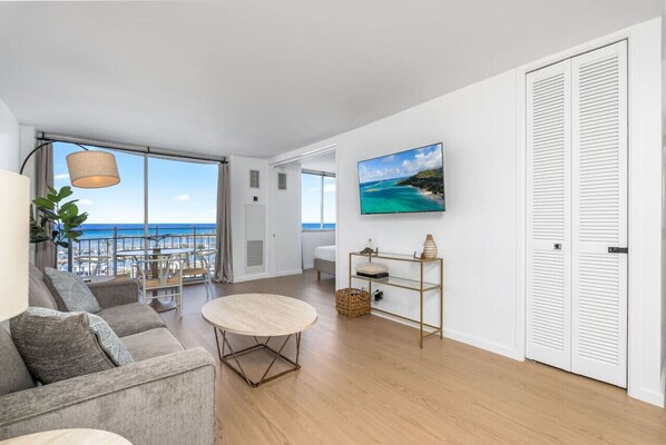 A modern living room with a view of the ocean, a round table, a sofa, and a mounted painting.