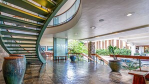 Un hall d’entrée spacieux, agrémenté d’un escalier en courbe, de grands pots de plantes et offrant une vue sur l’extérieur.